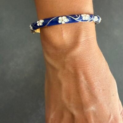 Bracelet jonc émaillé bleu marine à fleurs blanches porté au poignet, acier inoxydable doré