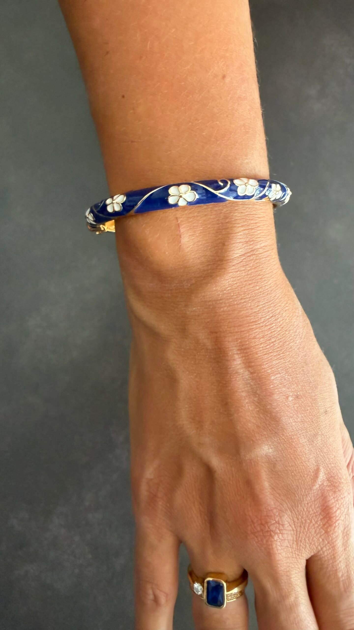 Bracelet Jonc Émaillé Bleu Marine Fleurs Blanches 1 Bracelet jonc émaillé bleu marine à fleurs blanches porté au poignet, acier inoxydable doré