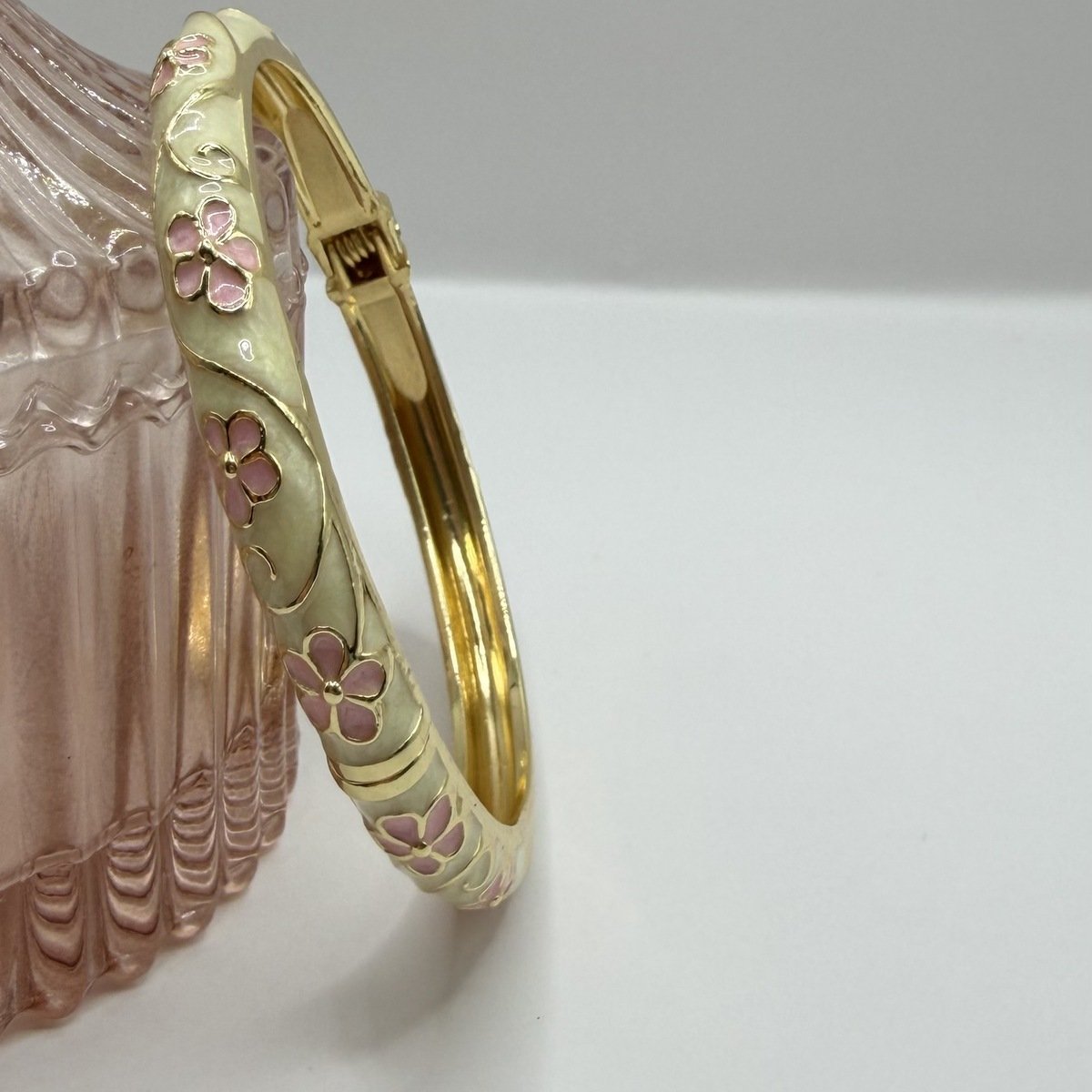 Bracelet Jonc Émaillé Fleurs Roses 5 Bracelet jonc émaillé crème à fleurs roses posé contre un pot en verre rose