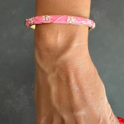 Bracelet jonc émaillé rose à fleurs blanches au poignet, charnière dorée visible
