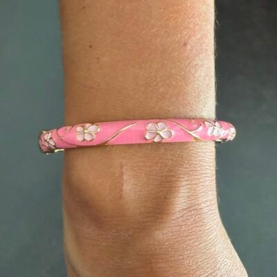 Bracelet jonc émaillé rose à fleurs blanches porté au poignet, acier inoxydable doré