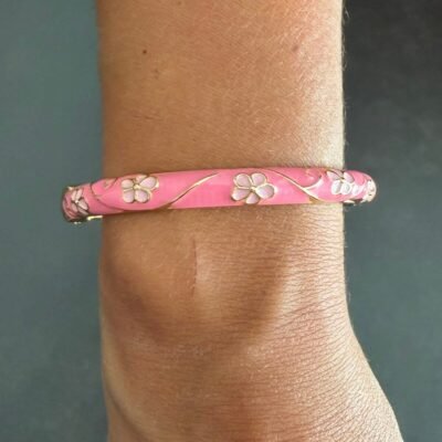 Bracelet jonc émaillé rose à fleurs blanches porté au poignet, acier inoxydable doré