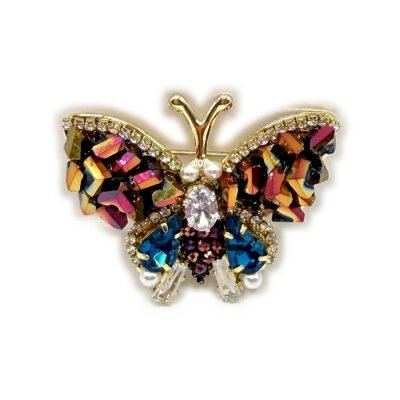 Détail des éclats de cristal iridescents et des gouttes bleu paon de la broche papillon