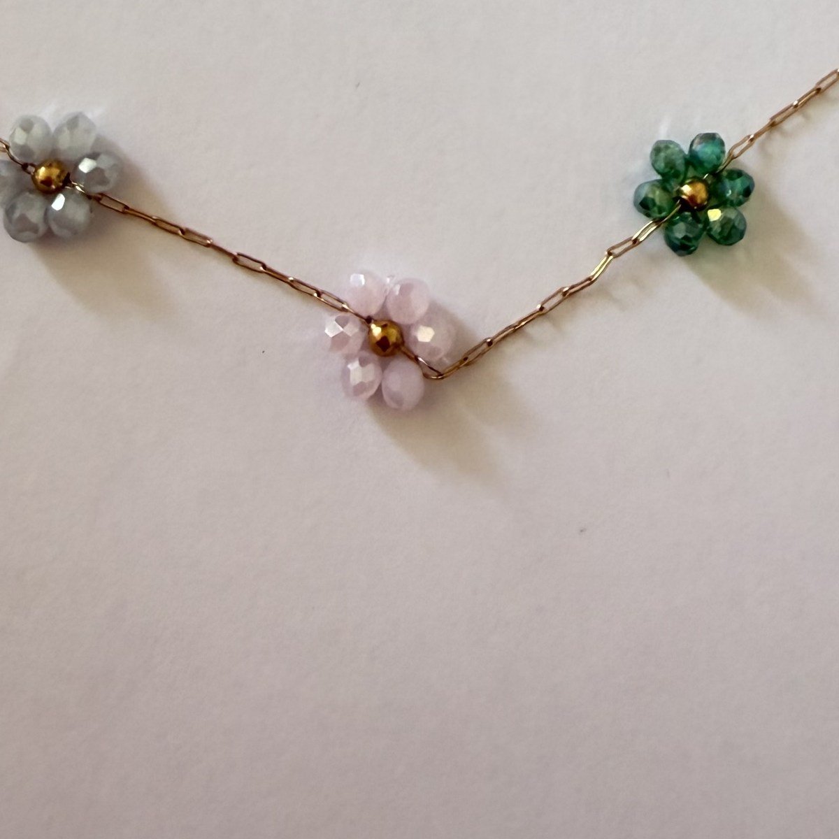 Collier Sept Fleurs Multicolores 3 Gros plan sur trois fleurs du collier : perles de cristal facettées gris, rose pâle et vert, cœur doré