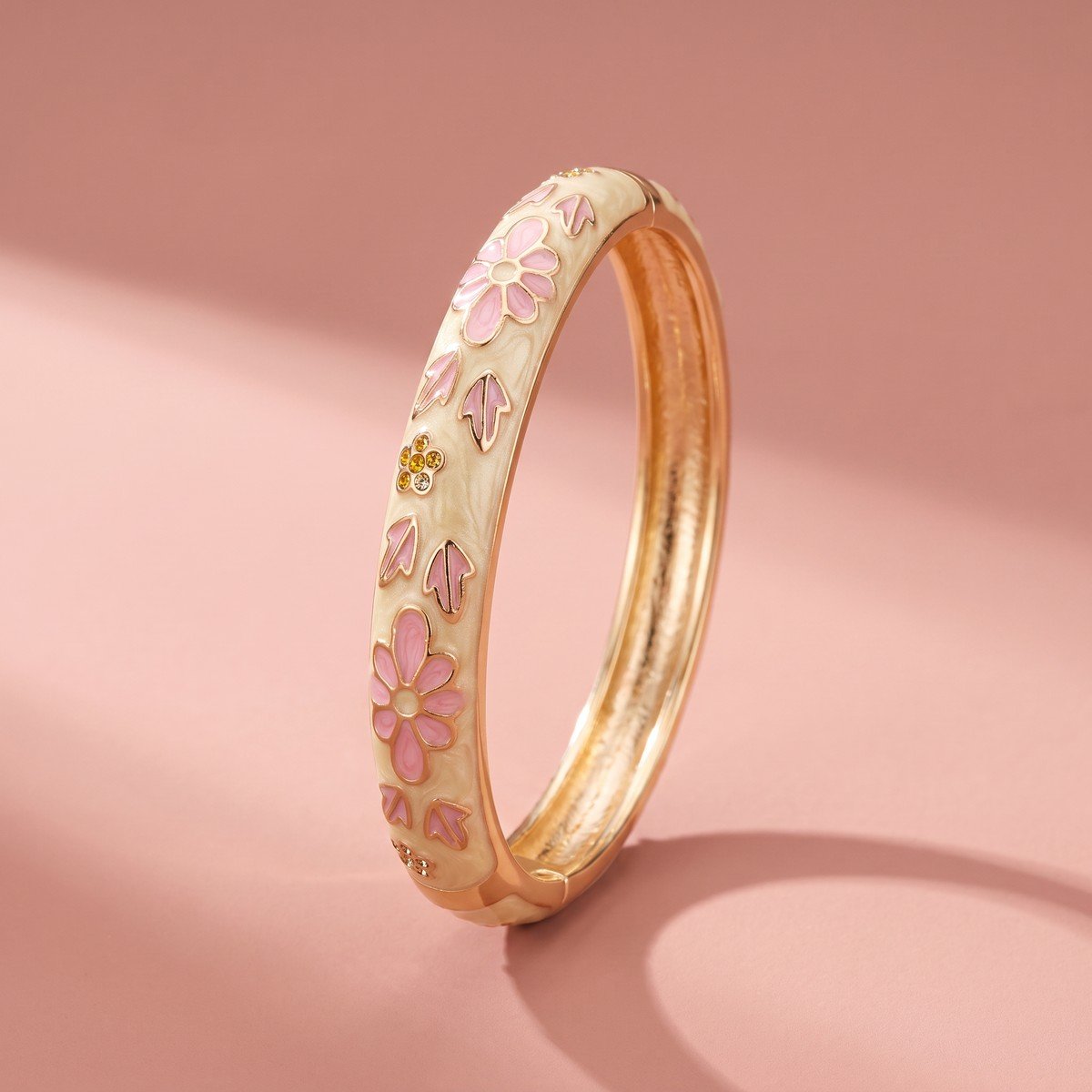 Bracelet Jonc Émaillé Fleurs Roses 1 Bracelet jonc émaillé fleurs roses en acier inoxydable doré, vue de trois quarts sur fond rose poudré
