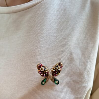 Broche papillon vert nacré portée sur un t-shirt blanc, vue avec le col