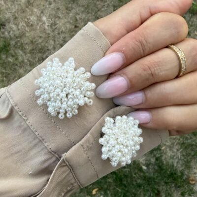 Paire de couvre-boutons perles nacrées portée sur les poignets d'une chemise beige
