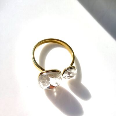 Bague ouverte dorée à deux cristaux posée sur un plateau blanc