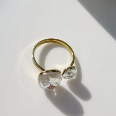 Bague ouverte dorée à deux cristaux posée sur un plateau blanc