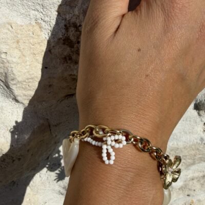Bracelet chaîne dorée à breloques nœud de perles, cœur nacré et fleur dorée porté, gros plan