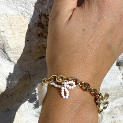 Bracelet chaîne dorée à breloques nœud de perles, cœur nacré et fleur dorée porté, gros plan