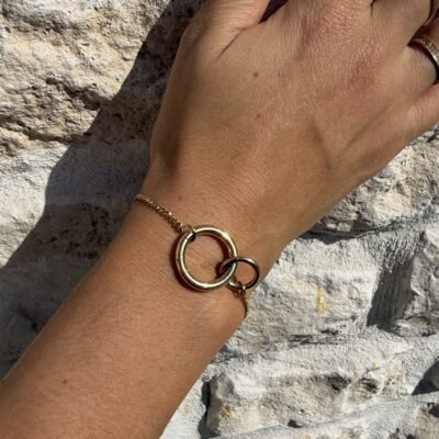 Bracelet anneaux entrelacés doré au poignet sur mur en pierre
