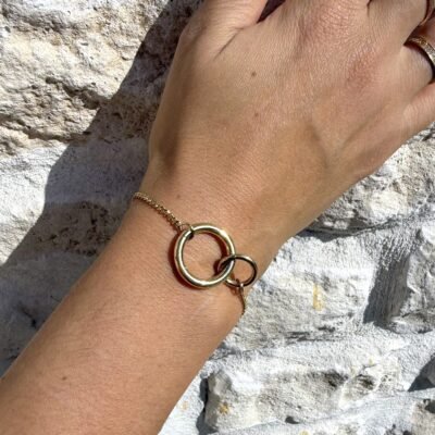 Bracelet anneaux entrelacés doré au poignet sur mur en pierre
