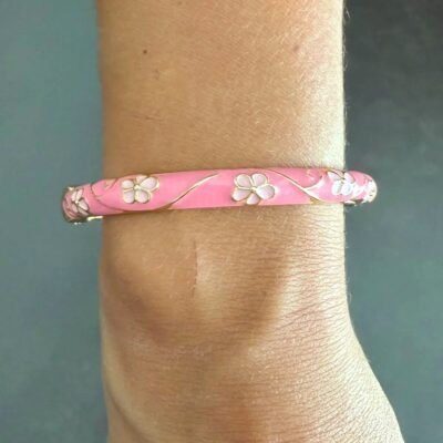 Bracelet jonc émaillé rose à fleurs blanches porté au poignet, acier inoxydable doré