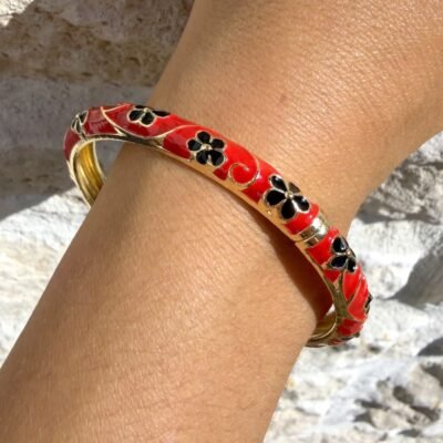 Bracelet jonc émaillé rouge à fleurs noires cernées d'or porté au poignet