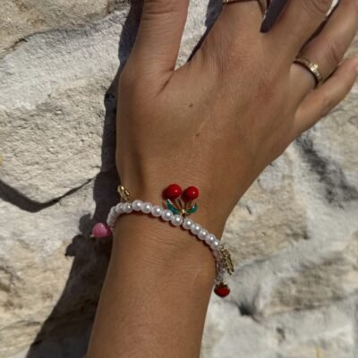 Bracelet perles et breloques cerises, cœur rose et trèfle porté sur un mur en pierre