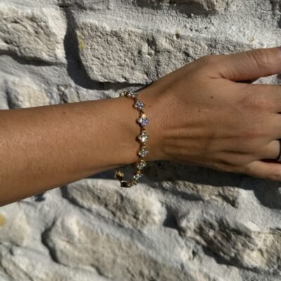 Bracelet trèfle strass doré porté contre un mur en pierre