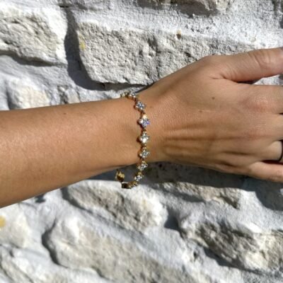 Bracelet trèfle strass doré porté contre un mur en pierre