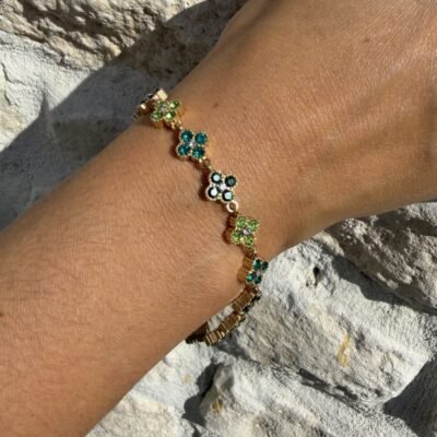 Bracelet trèfle vert doré porté contre un mur en pierre