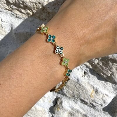 Bracelet trèfle vert doré porté contre un mur en pierre