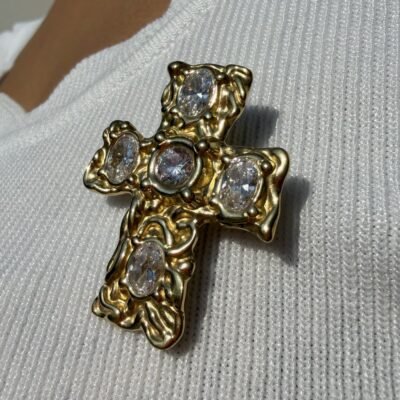 Broche croix baroque dorée à cristaux portée sur un top blanc, gros plan