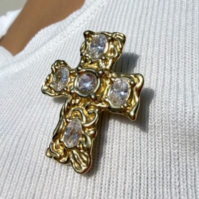 Broche croix baroque dorée à cristaux portée sur un top blanc, gros plan