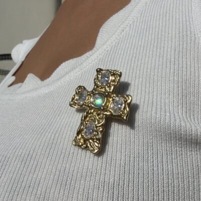 Broche croix baroque portée au soleil, reflets irisés sur le cristal central