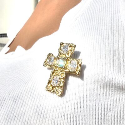 Broche croix baroque portée au soleil, reflets irisés sur le cristal central