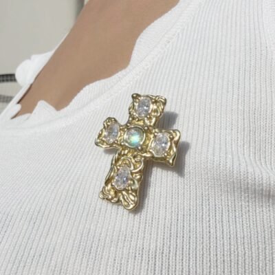 Broche croix baroque portée au soleil, reflets irisés sur le cristal central