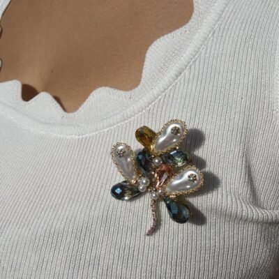 Broche fleur à pétales nacrés et cristaux bleus portée près du décolleté