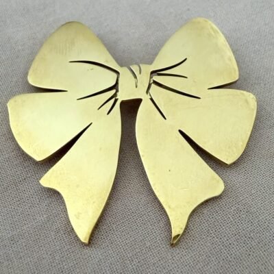 Broche nœud papillon dorée en acier inoxydable doré, vue de face sur fond de lin beige