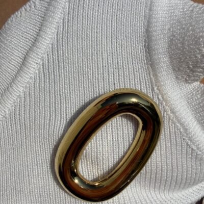 Broche ovale dorée portée sur un débardeur blanc côtelé, gros plan