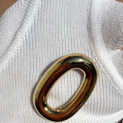 Broche ovale dorée portée sur un débardeur blanc côtelé, gros plan
