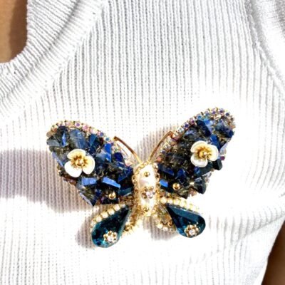 Broche papillon bleu nacré portée sur un top blanc, gros plan sur les fleurs de nacre