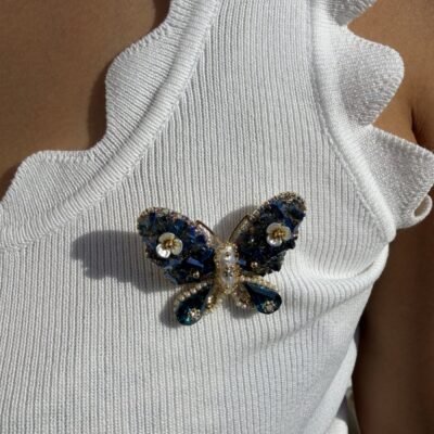 Broche papillon bleu à cristaux et gouttes bleu canard portée sur un débardeur blanc