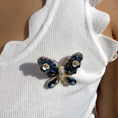 Broche papillon bleu à cristaux et gouttes bleu canard portée sur un débardeur blanc