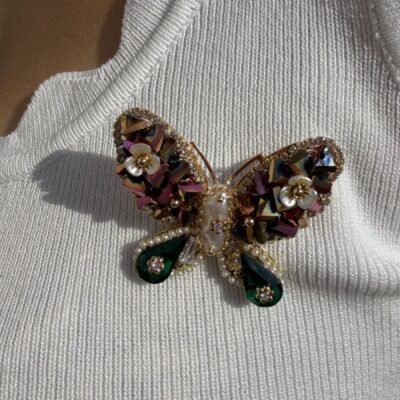 Broche papillon vert nacré portée au soleil sur un top blanc, gros plan