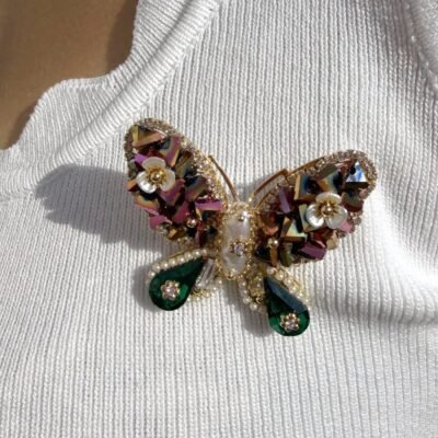 Broche papillon vert nacré portée au soleil sur un top blanc, gros plan