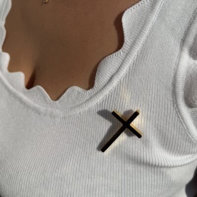 Pin's croix dorée porté sur un débardeur blanc avec collier fin doré