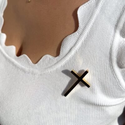 Pin's croix dorée porté sur un débardeur blanc avec collier fin doré